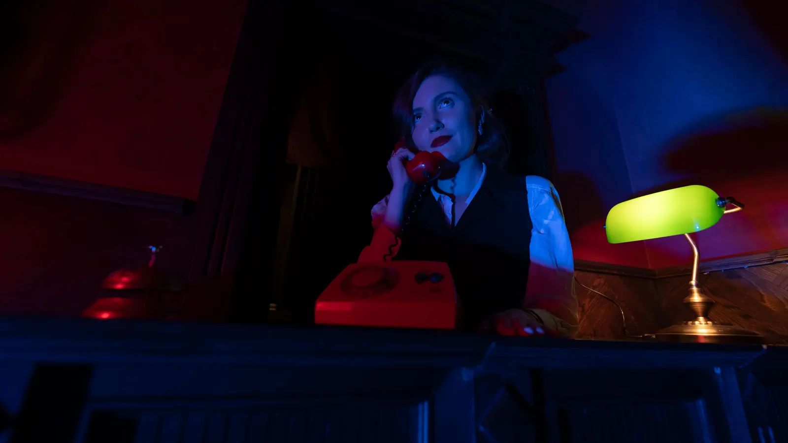 Recepcja Motelu California: kobieta przy czerwonym telefonie i zielona lampa na blacie